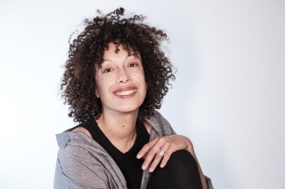 Stephanie Batten Bland smiles at camera while sitting on a table, left knee brought up to her chest