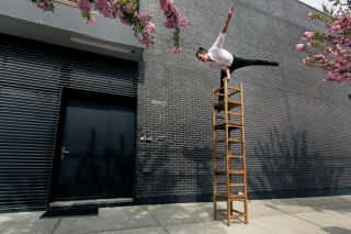 Person balancing on high stack of chairs.