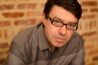 Portrait photo of a man in black framed glasses and a grey shirt