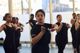 Dancers in black in front of windows.