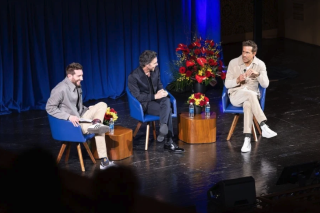 Three men sit on a stage. 