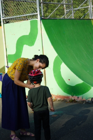 A mom puts a helmet on her child before he goes skateboarding.