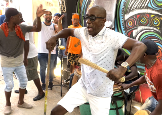 A person in all-white dancing with drummers