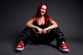 Dancer sits on floor. Wearing black leather pants and red and white sneakers.