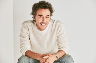 Shawn Levy wearingf white shirt and jeans, seated, smiling.