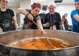 People gather around a large bowl of food. Chef stirs the orange food.